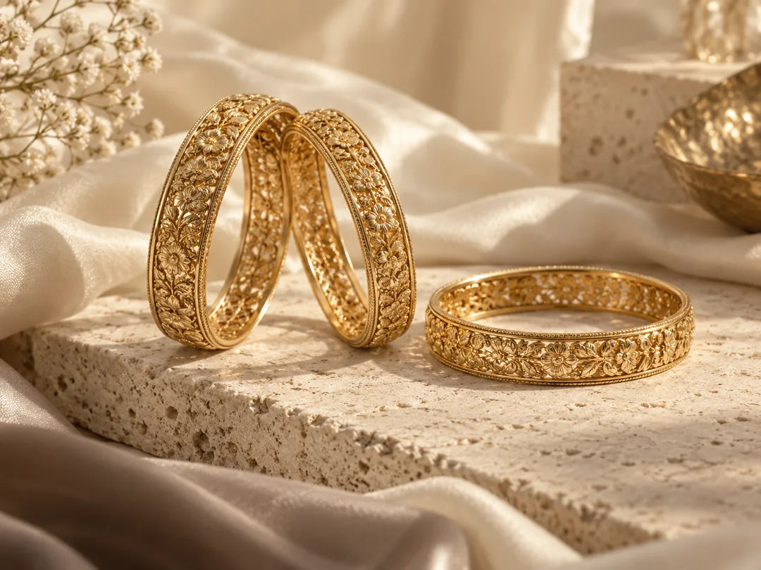 Three floral gold bangles arranged on travertine and champagne silk.