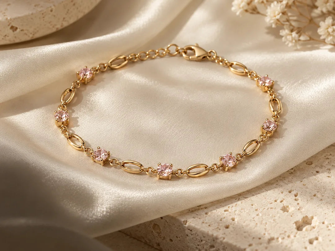 A fine gold chain bracelet with blush-pink gemstones on ivory satin.